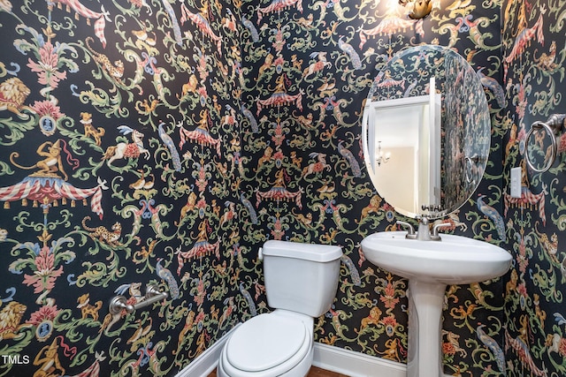 half bathroom with wallpapered walls, baseboards, and toilet