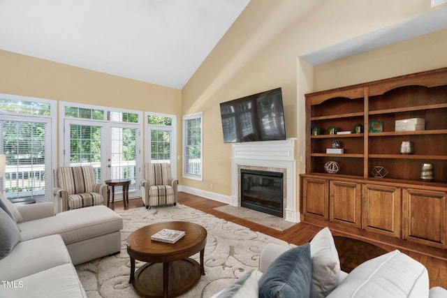 living room featuring baseboards, high vaulted ceiling, wood finished floors, and a tile fireplace