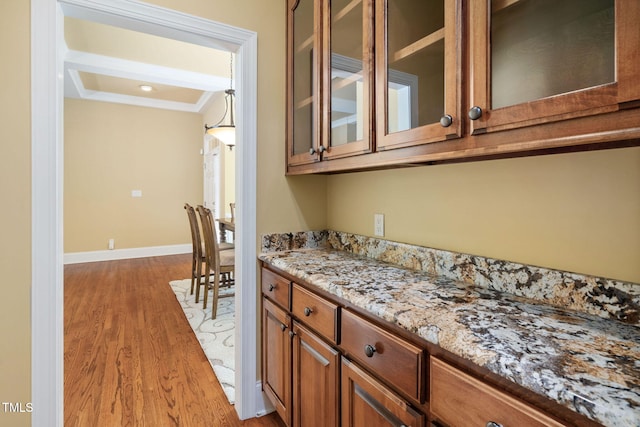 kitchen featuring light wood-style floors, glass insert cabinets, light stone countertops, and brown cabinets