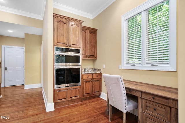 office area with baseboards, ornamental molding, built in desk, and light wood finished floors