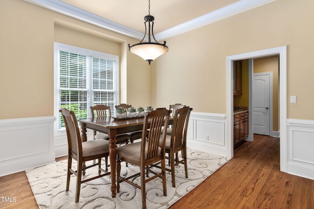 dining space featuring light wood-style floors, a wainscoted wall, ornamental molding, and a decorative wall