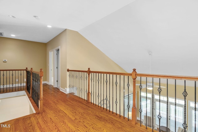 hallway with visible vents, wood finished floors, baseboards, recessed lighting, and vaulted ceiling