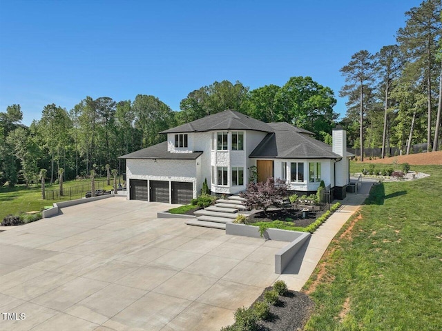 rear view of house with fence, a chimney, concrete driveway, an attached garage, and a yard