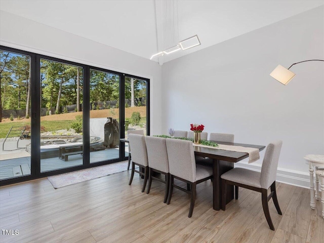 dining space featuring a towering ceiling, baseboards, a healthy amount of sunlight, and light wood-type flooring
