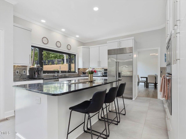 kitchen featuring a kitchen bar, recessed lighting, white cabinets, a sink, and backsplash