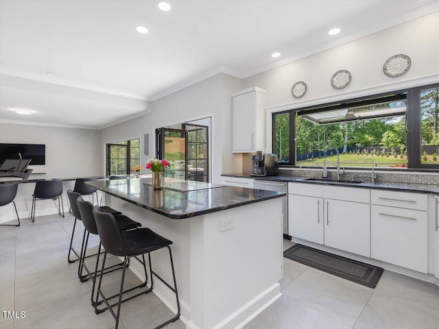 kitchen featuring a kitchen breakfast bar, a kitchen island, a sink, white cabinets, and dark stone counters