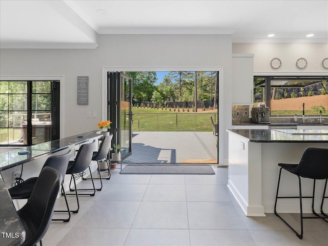 kitchen featuring a sink, light tile patterned floors, ornamental molding, a breakfast bar, and white cabinetry