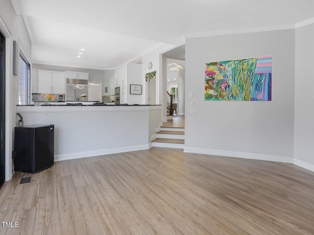 unfurnished living room featuring baseboards, ornamental molding, light wood-style flooring, and visible vents