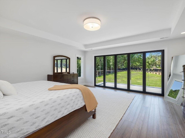 bedroom featuring a raised ceiling, visible vents, wood finished floors, and access to exterior