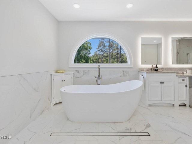 full bathroom featuring vanity, marble finish floor, wainscoting, a freestanding tub, and tile walls