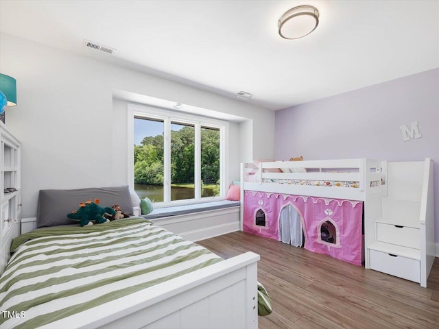 bedroom with visible vents, baseboards, a water view, and wood finished floors