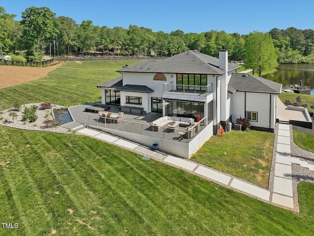 rear view of property featuring a shingled roof, an outdoor hangout area, a water view, a chimney, and a yard