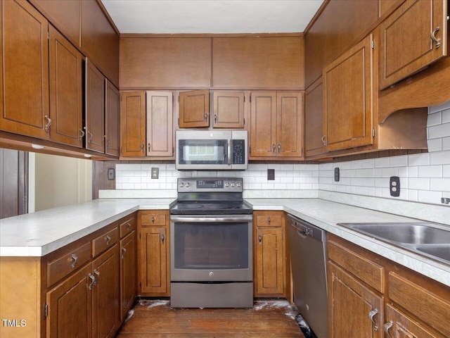 kitchen with appliances with stainless steel finishes, light countertops, dark wood finished floors, a peninsula, and tasteful backsplash