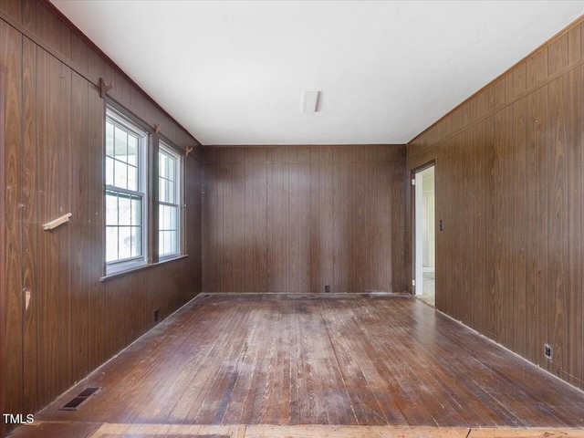 unfurnished room with wood-type flooring, wooden walls, and visible vents