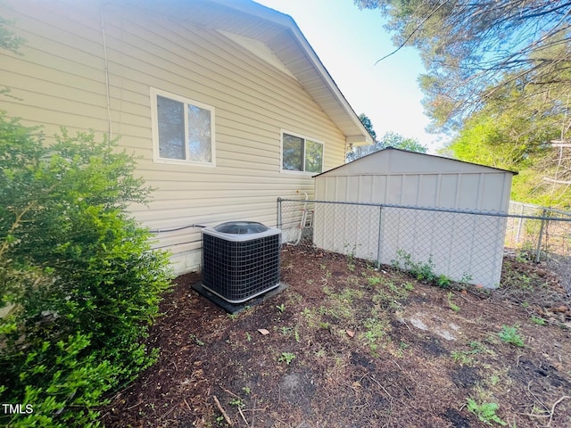 view of side of property with central AC, fence, an outbuilding, and a storage unit