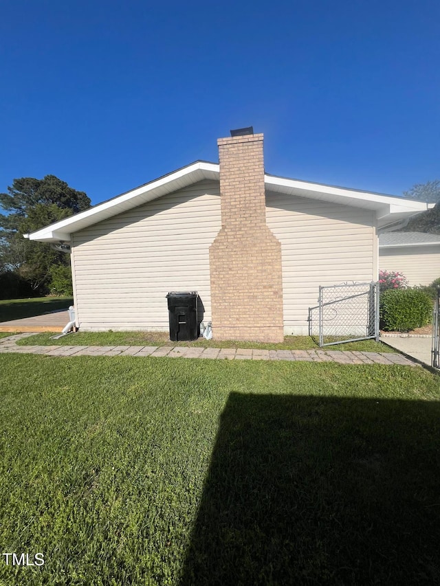 view of side of home featuring fence, a yard, a chimney, and a gate