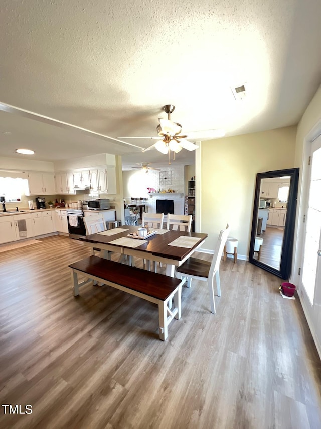 dining room featuring light wood-style floors, ceiling fan, a textured ceiling, visible vents, and baseboards