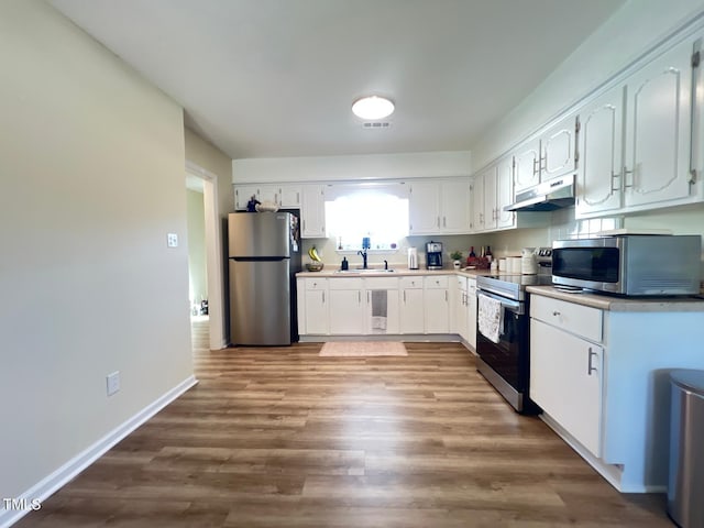 kitchen featuring white cabinets, under cabinet range hood, stainless steel appliances, a sink, and wood finished floors