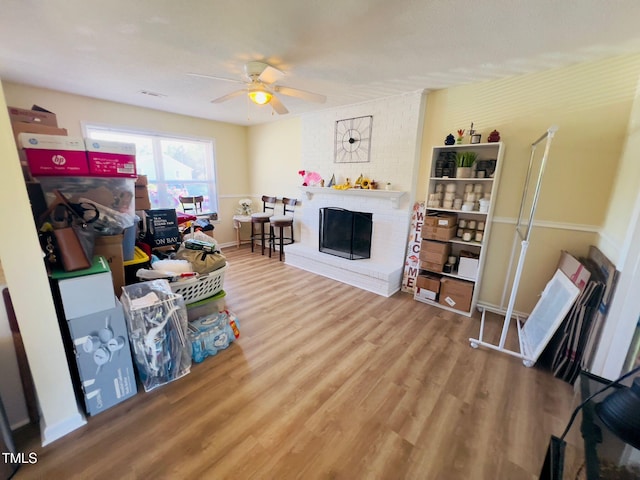 living room featuring ceiling fan, a brick fireplace, wood finished floors, and baseboards