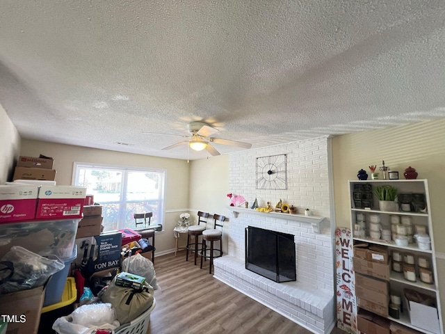 living room featuring a brick fireplace, a ceiling fan, wood finished floors, and a textured ceiling