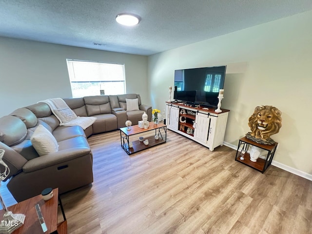 living room with light wood-style flooring, a textured ceiling, baseboards, and visible vents