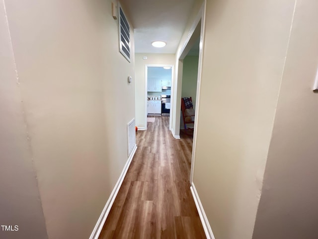 hallway featuring wood finished floors, baseboards, and visible vents