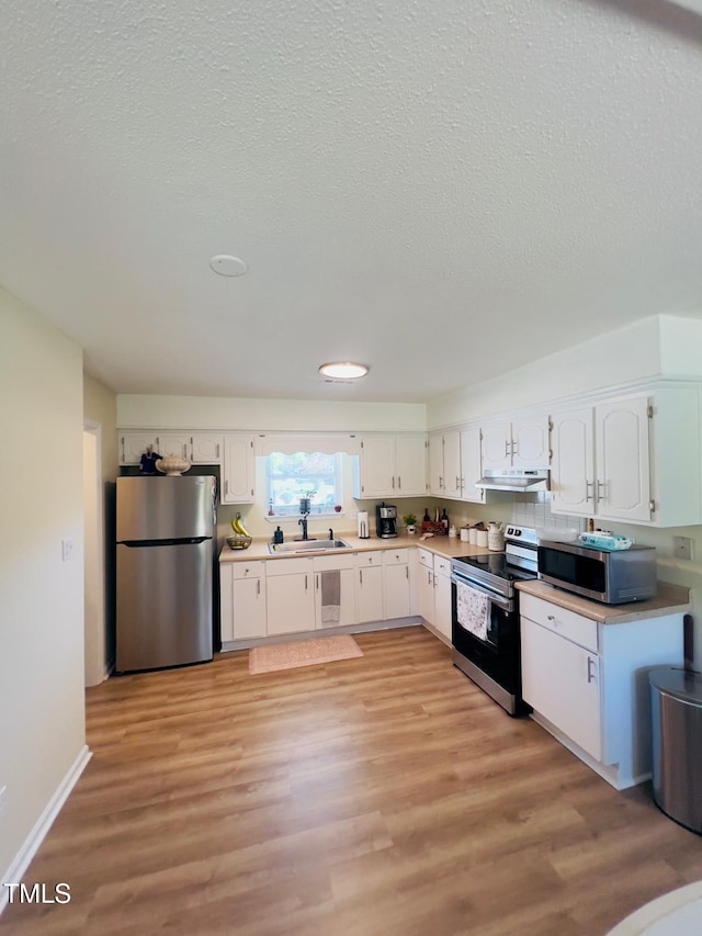 kitchen featuring light countertops, white cabinets, under cabinet range hood, stainless steel appliances, and a sink
