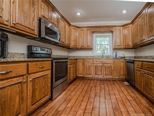 kitchen featuring a sink, appliances with stainless steel finishes, brown cabinetry, and wood-type flooring