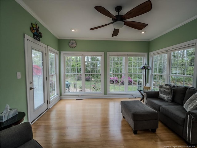 living area featuring ornamental molding, light wood finished floors, ceiling fan, and a healthy amount of sunlight
