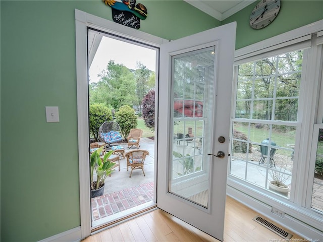 entryway with visible vents, ornamental molding, and light wood-type flooring