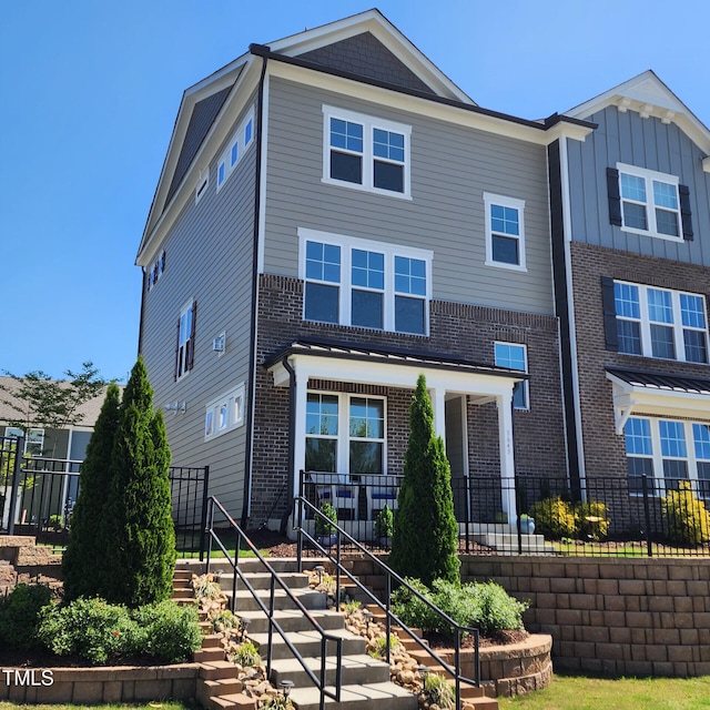 view of front of home featuring brick siding, fence, stairs, and covered porch