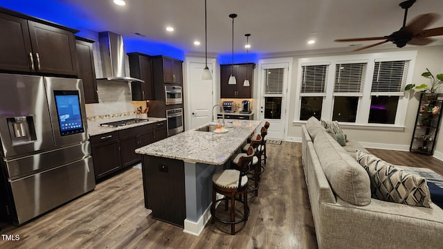 kitchen with wall chimney range hood, a breakfast bar area, appliances with stainless steel finishes, a sink, and dark wood-type flooring