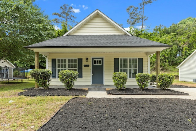 bungalow featuring a porch, a trampoline, roof with shingles, and a front lawn