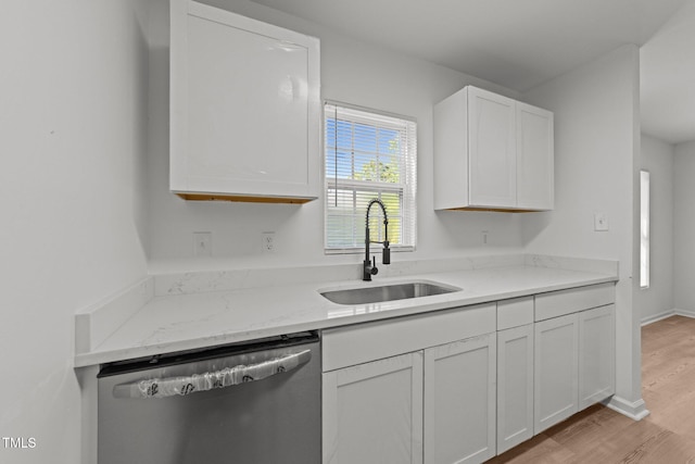kitchen featuring stainless steel dishwasher, white cabinetry, light stone counters, a sink, and light wood finished floors