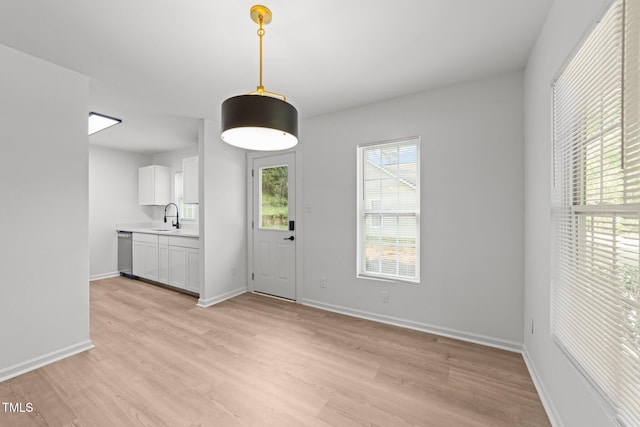 unfurnished dining area featuring light wood-style floors, a sink, and baseboards