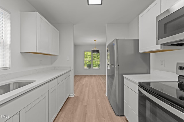 kitchen featuring appliances with stainless steel finishes, light wood-style flooring, white cabinetry, and light stone countertops