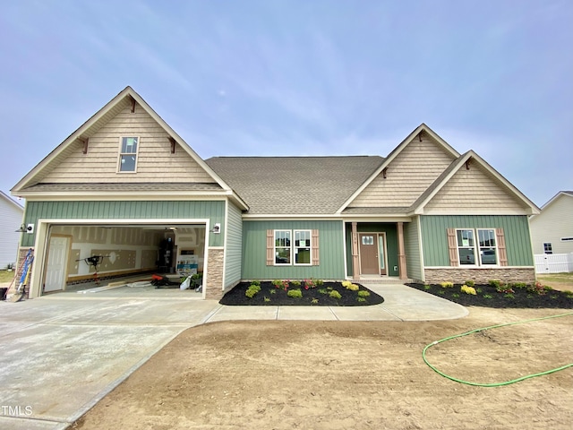 craftsman-style home featuring stone siding, concrete driveway, roof with shingles, and a garage