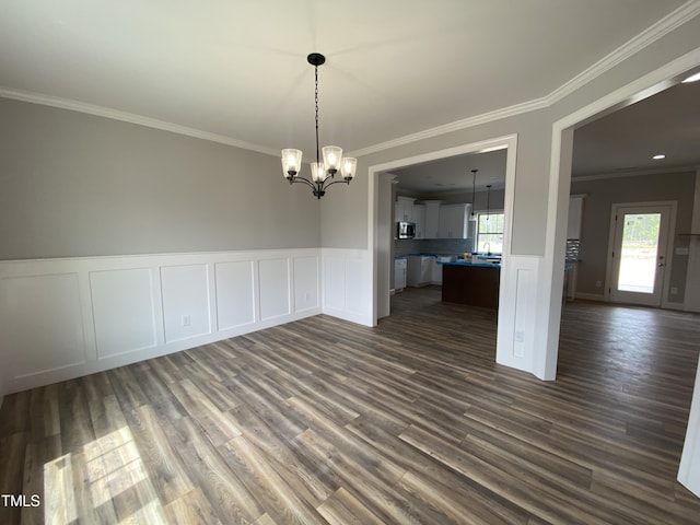 unfurnished dining area with a decorative wall, a notable chandelier, wainscoting, dark wood finished floors, and ornamental molding