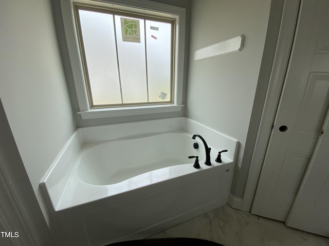 bathroom featuring a garden tub, marble finish floor, and a wealth of natural light