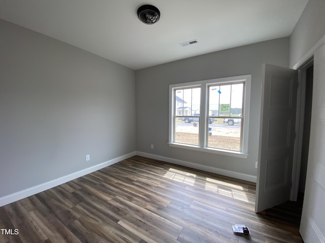 unfurnished room with baseboards, visible vents, and dark wood-style floors