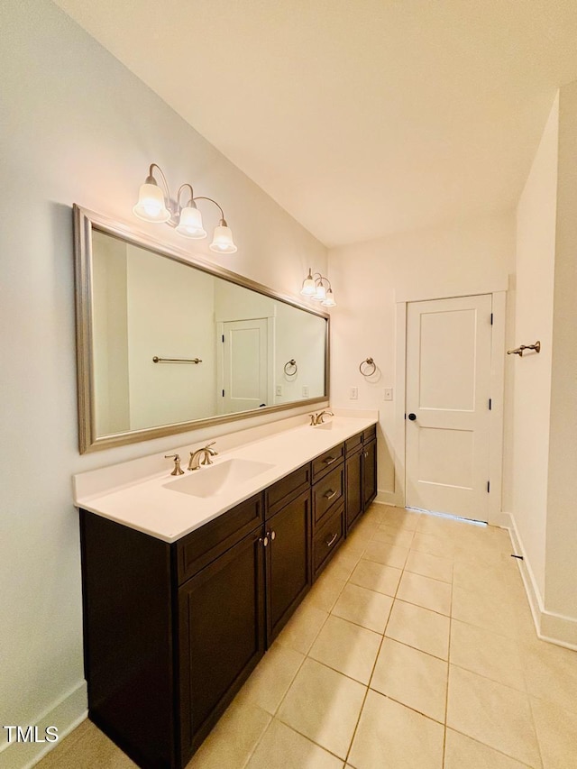 bathroom with baseboards, tile patterned flooring, double vanity, and a sink
