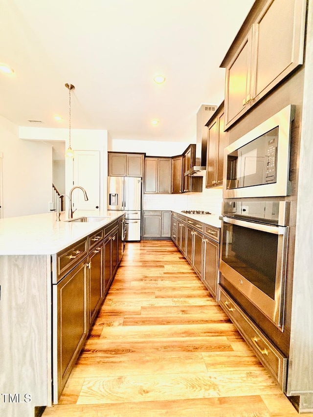 kitchen featuring a sink, stainless steel appliances, light wood-type flooring, an island with sink, and light countertops