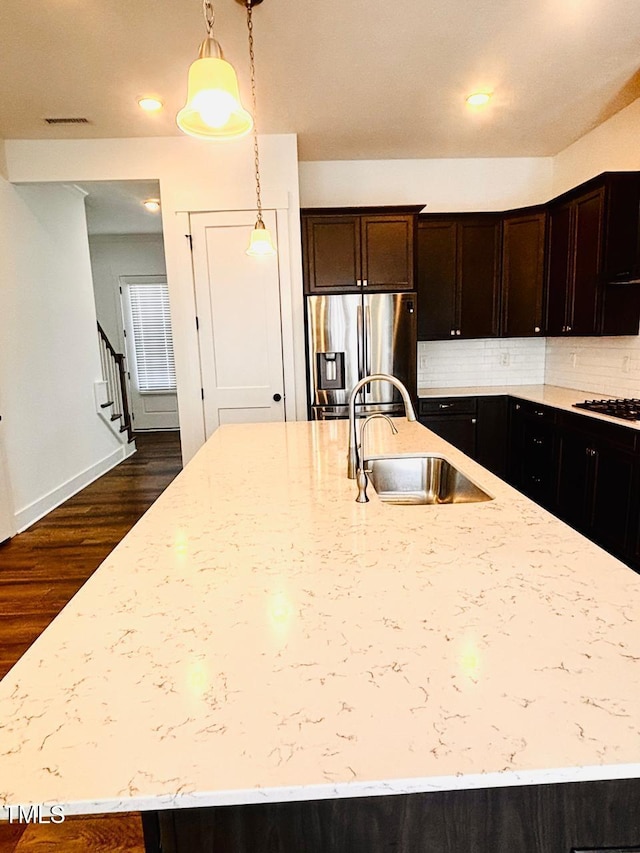 kitchen with stainless steel fridge, a sink, decorative backsplash, a spacious island, and light stone counters