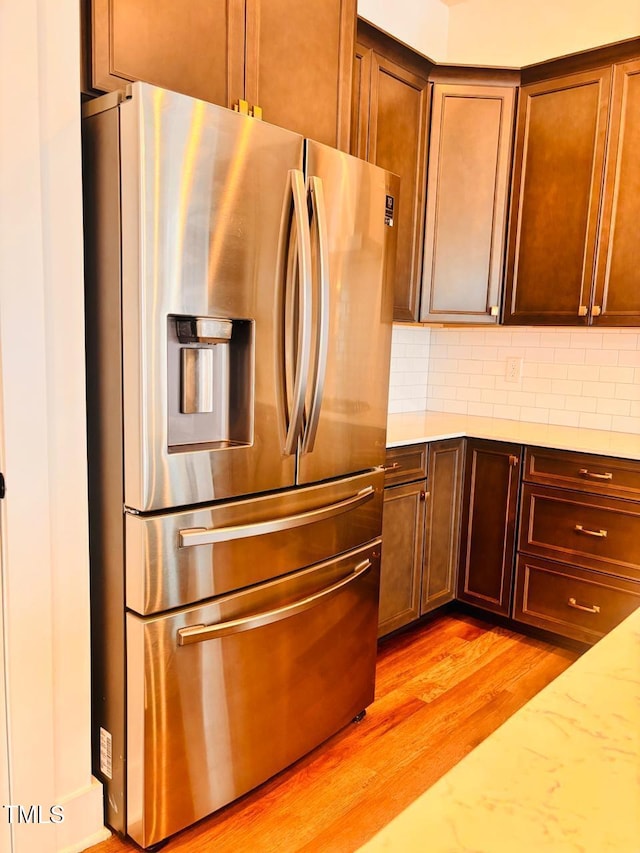 kitchen featuring light stone counters, decorative backsplash, stainless steel fridge, and light wood-style flooring