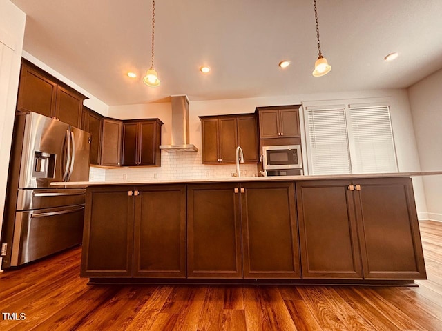 kitchen featuring wall chimney range hood, decorative light fixtures, backsplash, dark wood-style floors, and appliances with stainless steel finishes