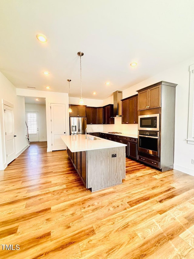 kitchen featuring light countertops, wall chimney exhaust hood, stainless steel appliances, and light wood-style floors