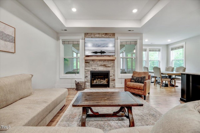 living area with a large fireplace, a tray ceiling, wood finished floors, and visible vents