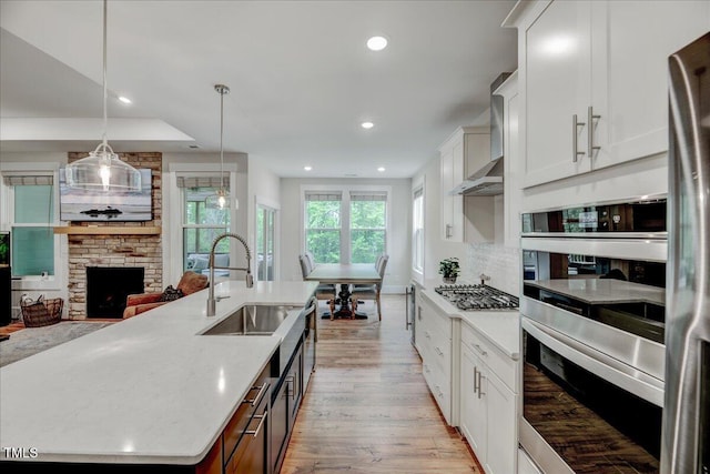 kitchen featuring stainless steel appliances, light wood-style flooring, a sink, white cabinetry, and wall chimney range hood