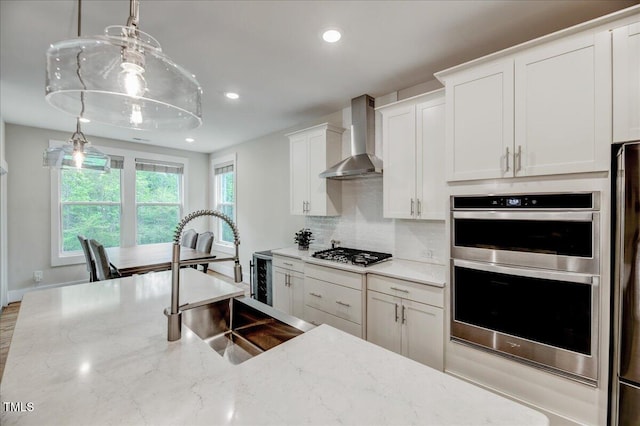 kitchen with a sink, recessed lighting, wall chimney range hood, gas stovetop, and double oven