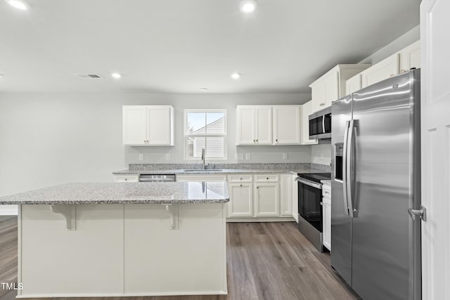 kitchen with a kitchen breakfast bar, visible vents, appliances with stainless steel finishes, a sink, and dark wood-style floors